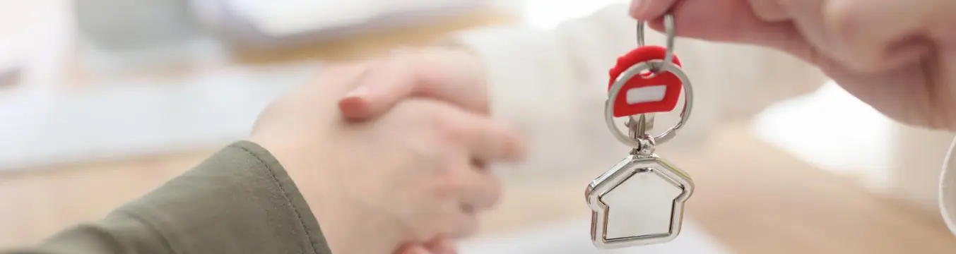 Entrega de llaves con un llavero en forma de casa mientras dos personas se dan la mano