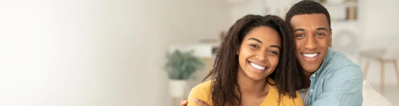 Pareja sonriente abrazada en la sala de su vivienda