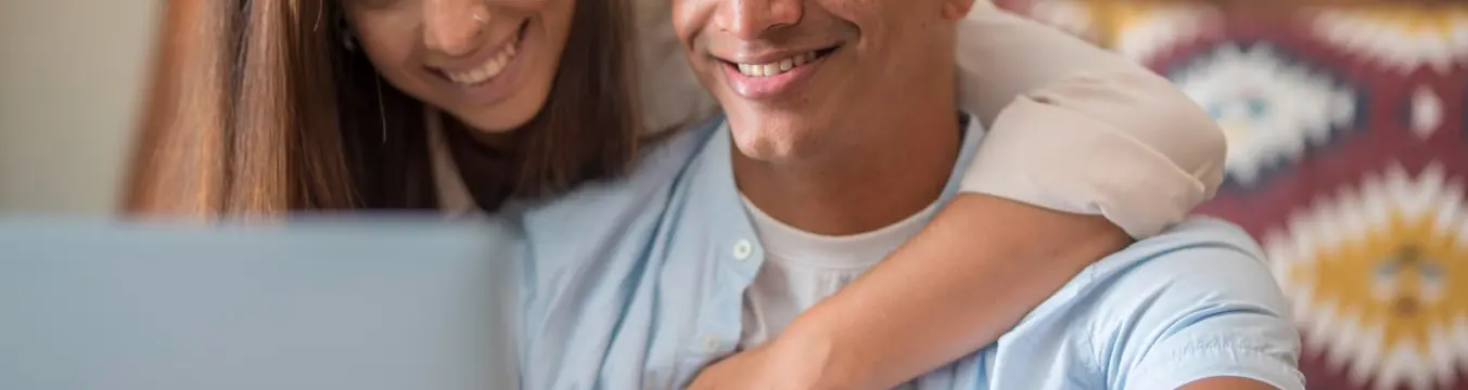 Pareja sonriente mirando un portátil en casa
